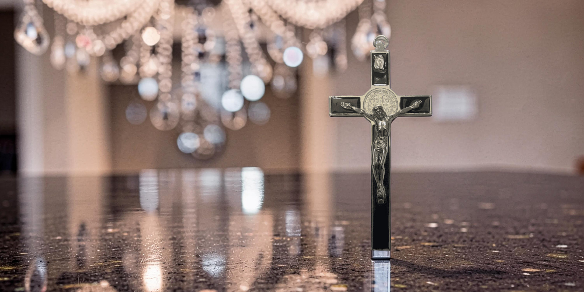 St. Benedict crucifix on black marble table with chandelier in the background